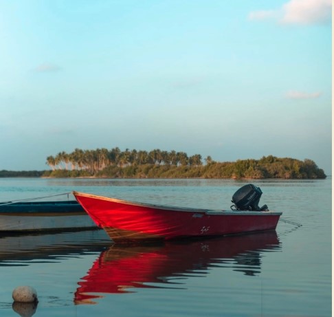 The image shows a red motor boat anchored near a quay. There is a small buoy floating near it. In the distance you can see a small island.